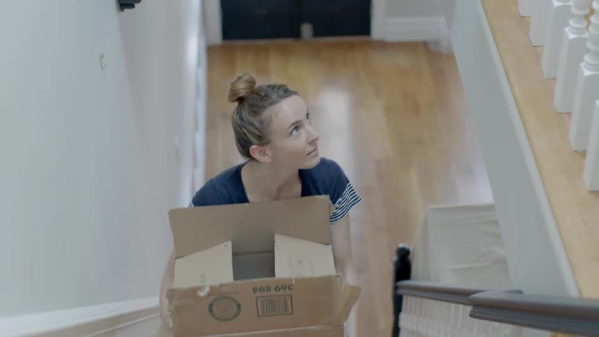 Woman smiling and carrying a box up stairs