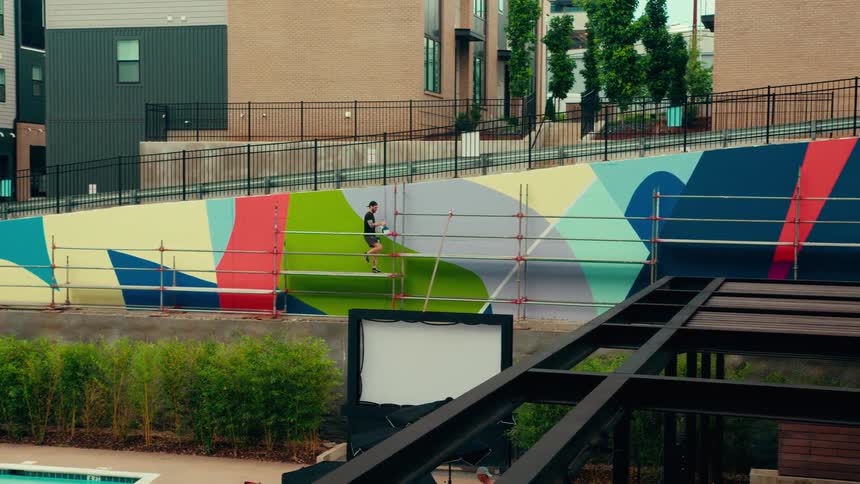 Person walking in front of a colorful geometric mural with scaffolding in an urban area