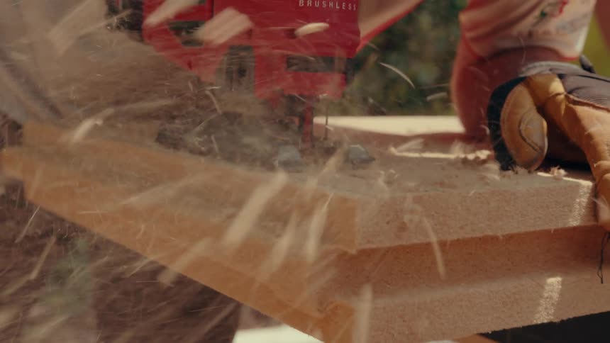 A closeup shot shows a red jigsaw cutting through a thick lightcolored insulation panel sending sawdust flying through the air