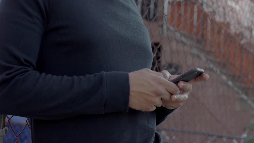 A man is using a phone by a fence