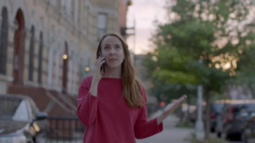 A woman is walking in her neighborhood and arguing on a cellphone