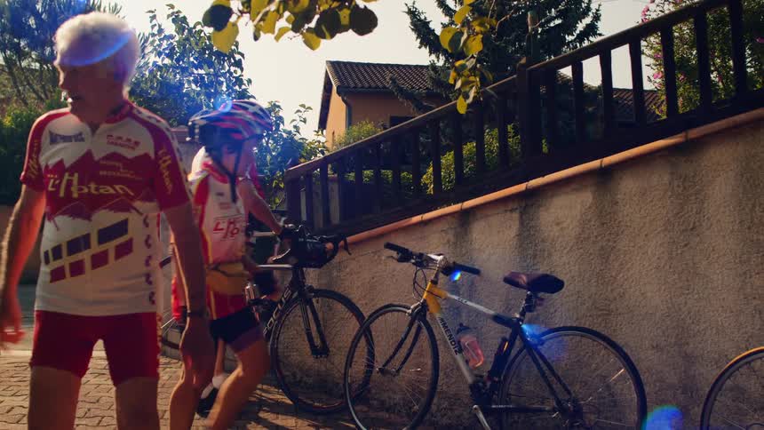 Group of cyclists in red and white uniforms beside stone wall in sunny residential area