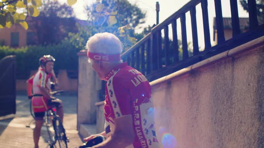 Cyclists in red and white uniforms preparing for ride in sunlit residential area