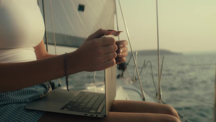 A woman sits on a boat holding a laptop on her lap as the boat travels on the ocean