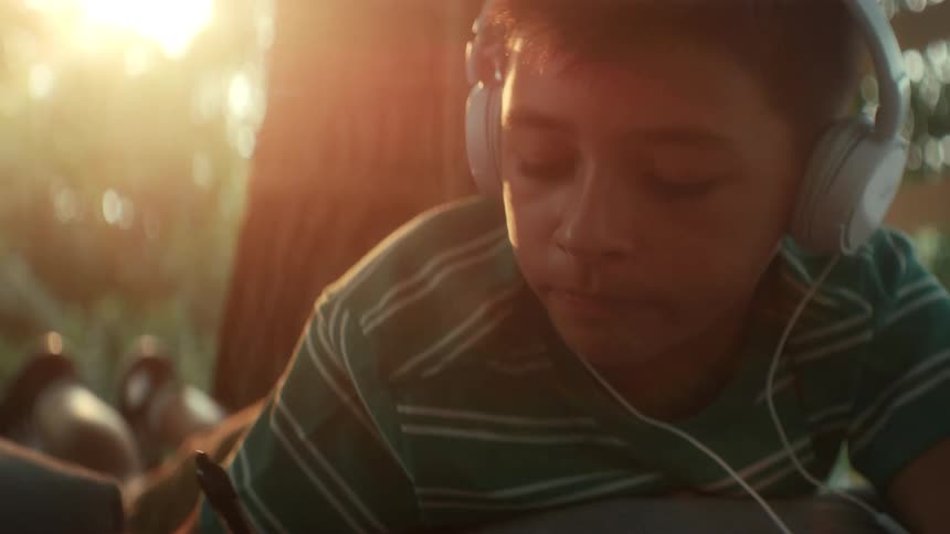 Person in green and white striped shirt is writing in a notebook diligently taking notes while listening with earphones