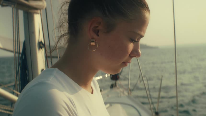 Young woman sits on a boat sailing off the coast as she looks up