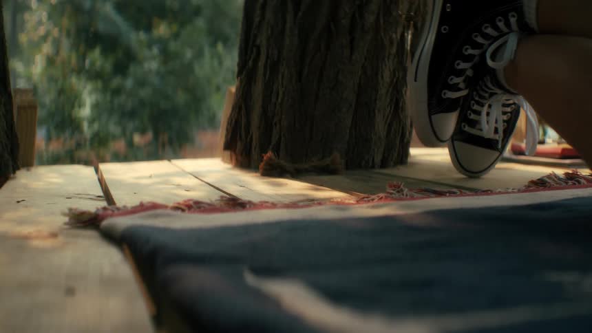 A carefree young person swings their feet whie listening to music outside duirng the summer in their treehouse