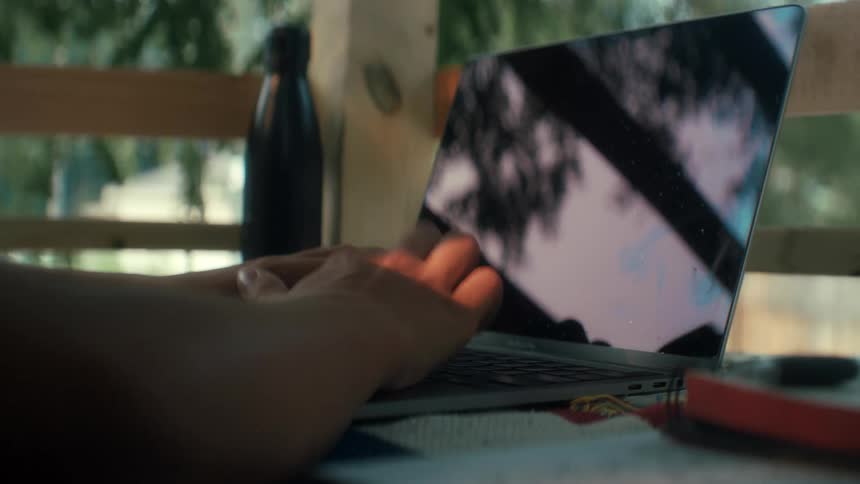 A young person typing on their laptop outside doing work or schoolwork or homework