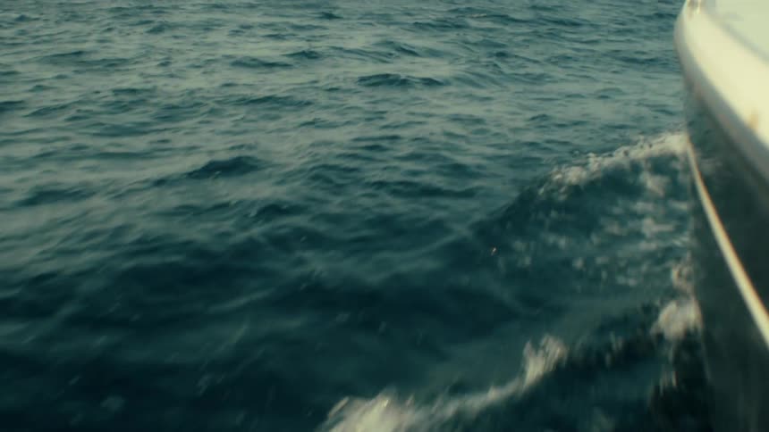 A motorboat cuts through dark blue water leaving a white wake under a clear sky looking forward with steady momentum