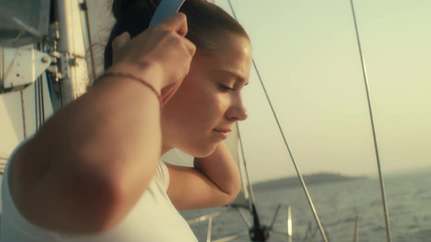 Teenage girl moves headphones from around her neck to her ears while sailing on a boat