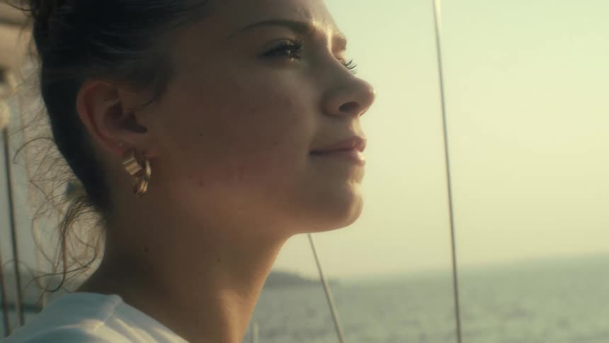 Young woman sits on a boat sailing off the coast as she looks up