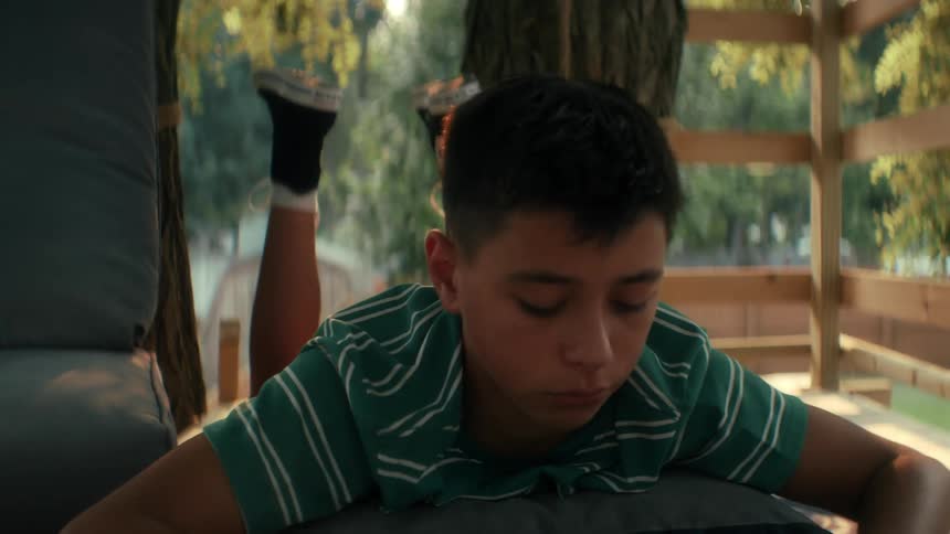 Young boy taking off headphones in his treehouse and closing his laptop computer before standing up and finishing his homework