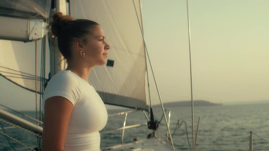 Young woman sits on a boat sailing off the coast as she looks up from her laptop computer