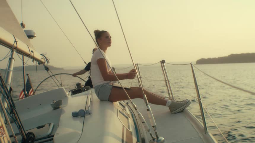 Woman sitting on a sailboat deck sailing on calm waters at sunset