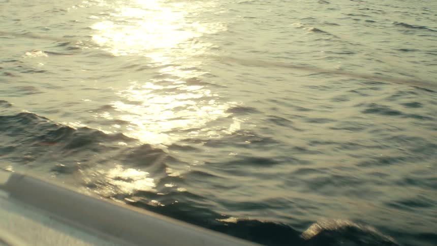 View from a boat sailing as sunlight shines on the ripples and waves of the water