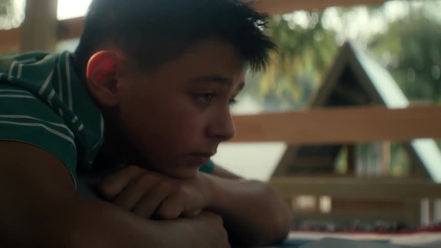 Boy lies on his stomach on a wooden deck outdoors thinking during the daytime