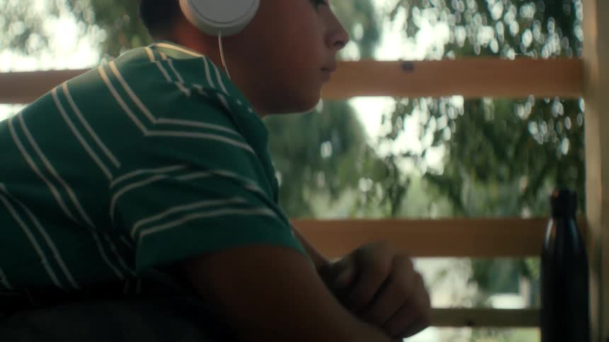 Boy lying down outside putting on white headphones to listen and watch