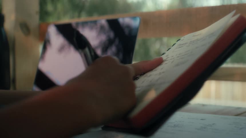 A boy picking up a pen and writing notes in a notebook