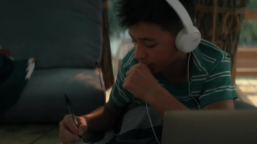 Boy writing and using a laptop while listening to music or a podcast
