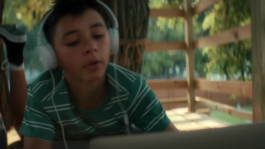 A boy opens a laptop and puts on headphones to start his homework