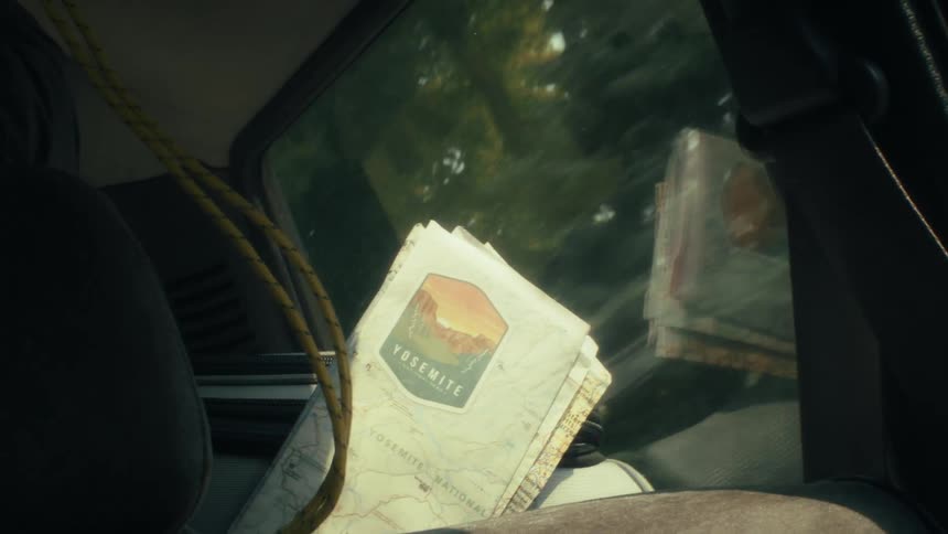 A car drives along at midday seen through the windows as trees blur past outside on the back seat a bag and a few loose pieces of paper rest against the upholstery