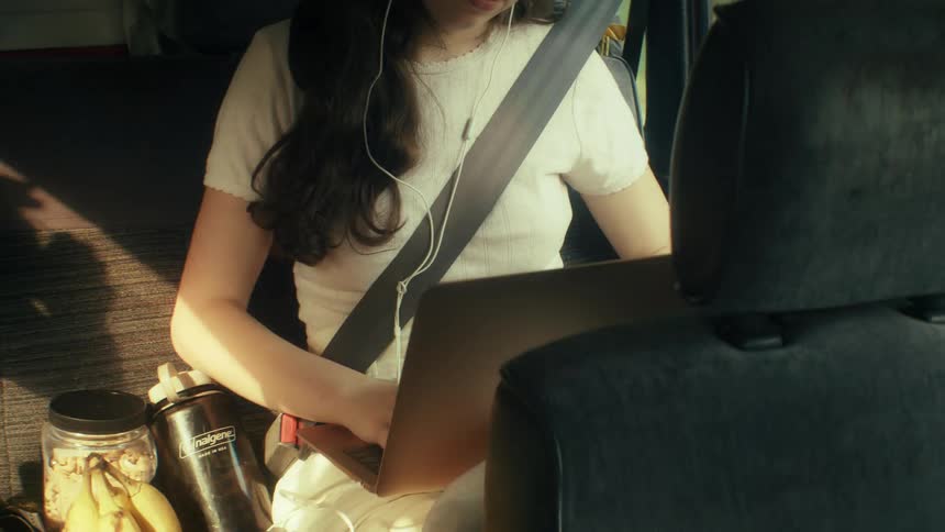 The girl is riding in the backseat typing on a laptop