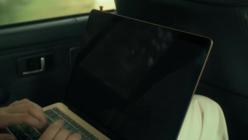 Hands of a teenage girl typing on the keyboard of a laptop computer as she sits in the back seat of an automobile