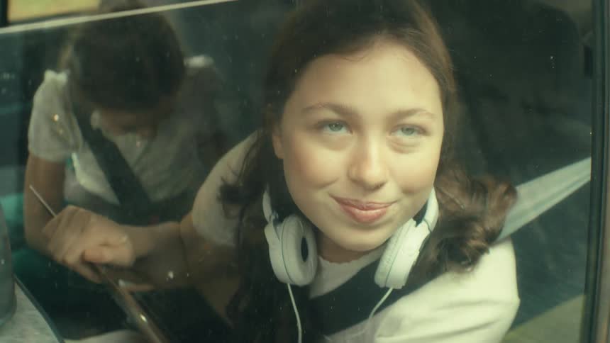 Person looks out window with slight smile and headphones around neck