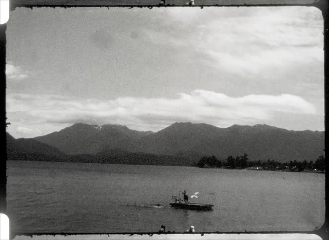 People jumping from a wooden deck towards the sea with mountains in the background