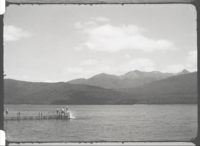 People are diving off the pier into the lake