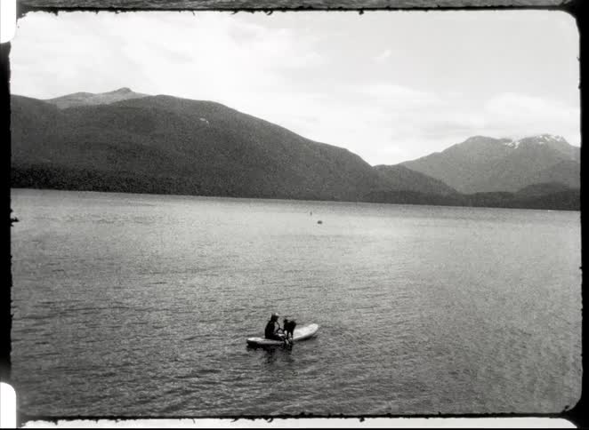 Person with a dog in a kayak on a lake with mountains in the background