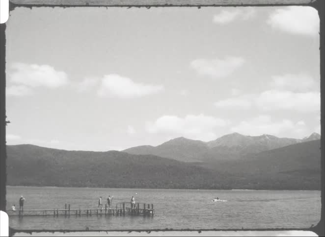 People on a wooden pier by the sea with mountains in the background