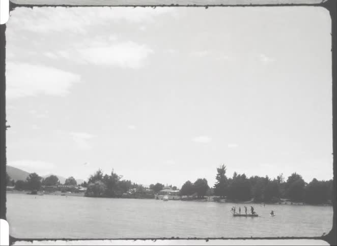 A group of people stands on a boat riding across a lake at midday