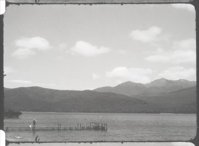 Person stands on wooden dock with mountains in the background