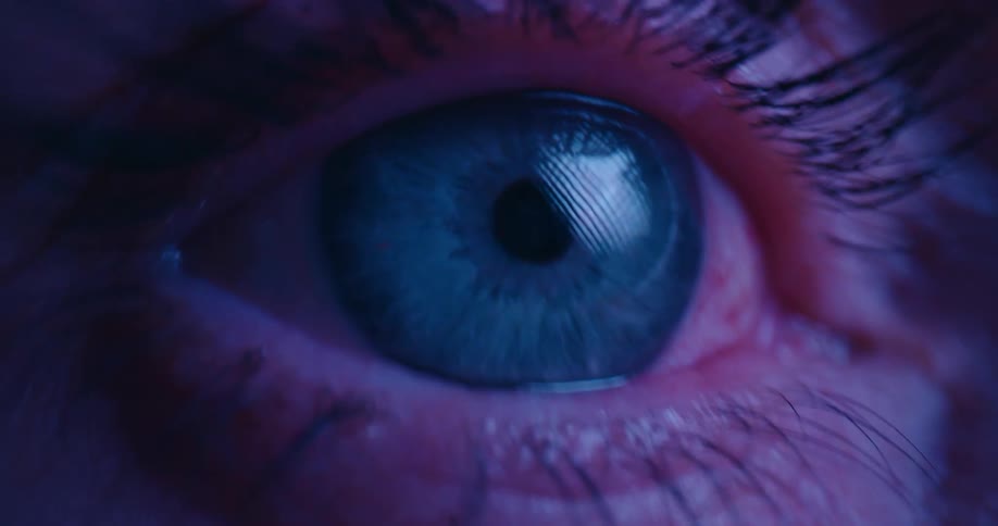 Rapidly changing colored lights flash across an extreme close up of a blue eye