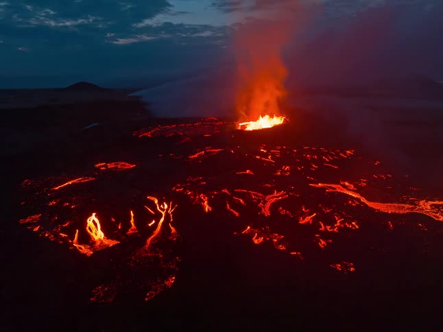 Smoke and flames emerge from an erupting volcano as molten hot lava moves across the land