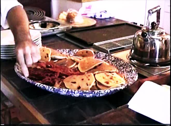 The man picks up a piece of bacon and eats it