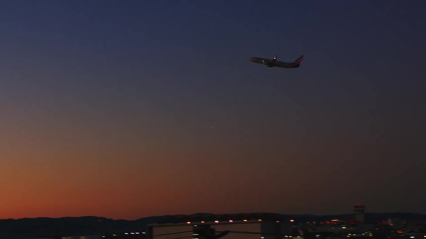 An airplane takes off from a bustling airport ascending into the twilight sky and soaring gracefully across a stunning sunset gradient above distant mountains