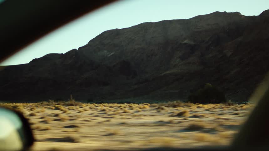 View from an open car window traveling by mountains in the desert