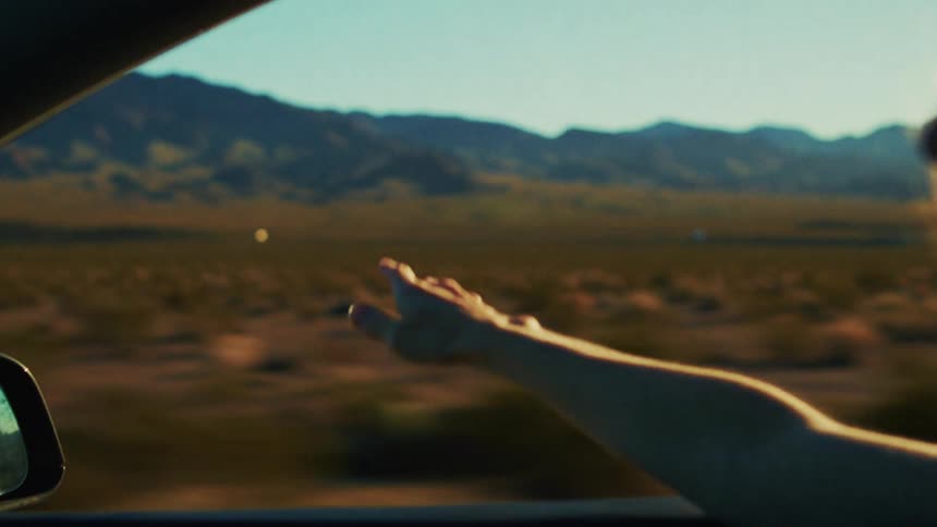 The woman waves her arm out of the moving cars window