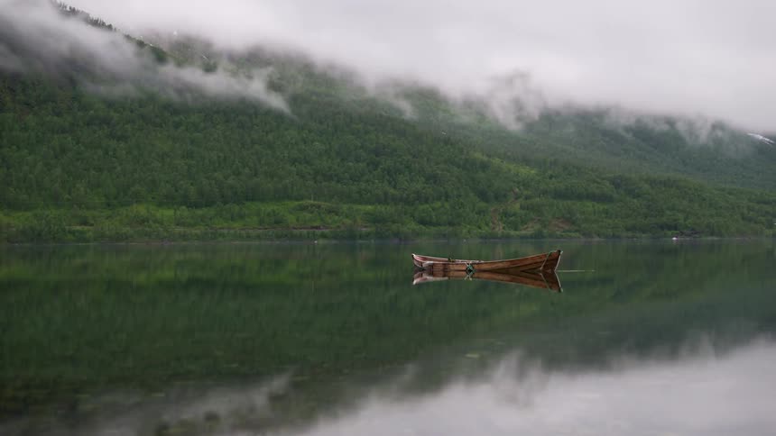 The empty wooden rowboat floats in the foggy lake