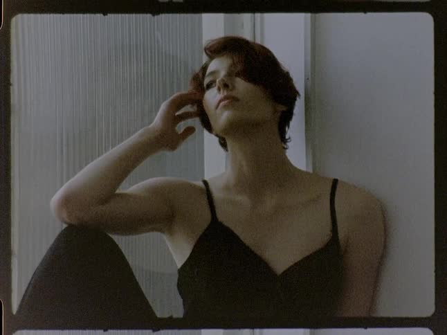 Woman sitting rests her head on one hand beside a wall indoors