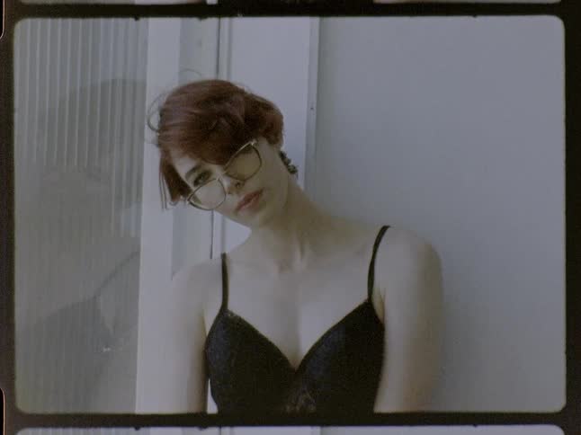 Woman wearing glasses and a black top tilts her head back beside a wall indoors