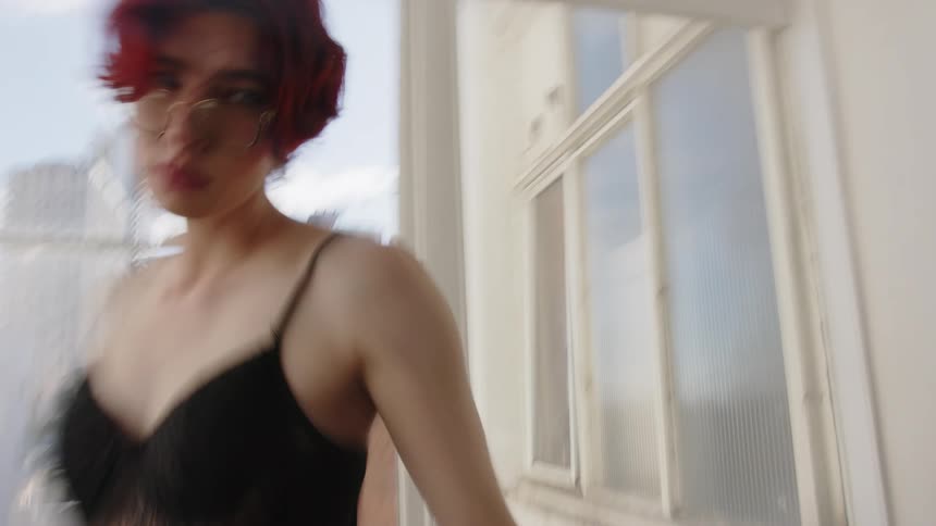 Woman walks beside a window and appears blurred in an indoor space with buildings in the background