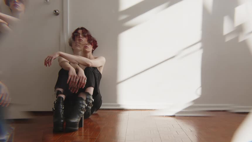 Woman sitting on the floor hugs her legs against a wall under natural light indoors