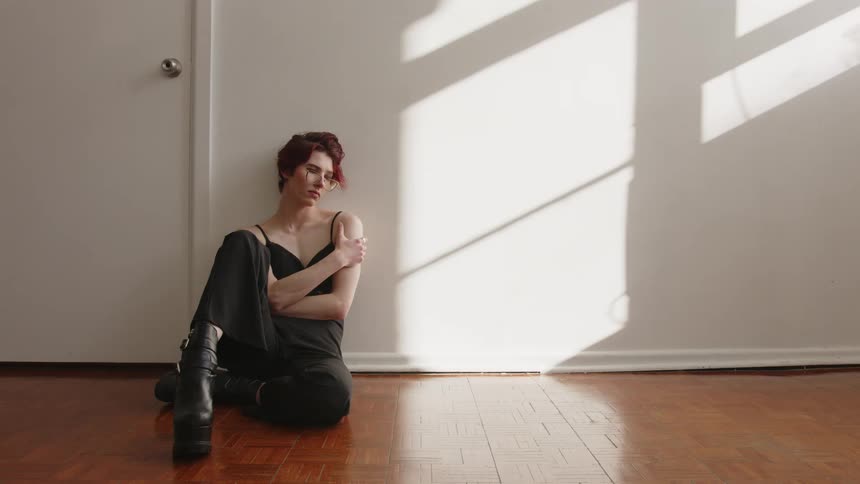 Woman sitting on the floor crosses her arms and looks to the side under natural light indoors