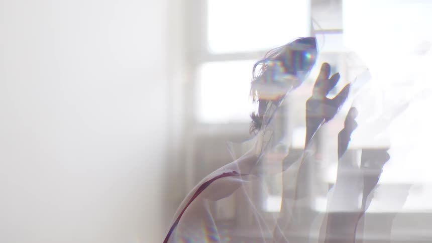 Woman wears a reflective geometric mask and tilts her head under diffused light indoors