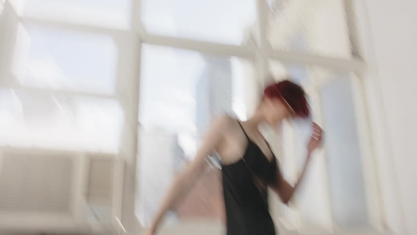 Woman standing in front of a window appears blurred in an indoor space with chairs and buildings in the background