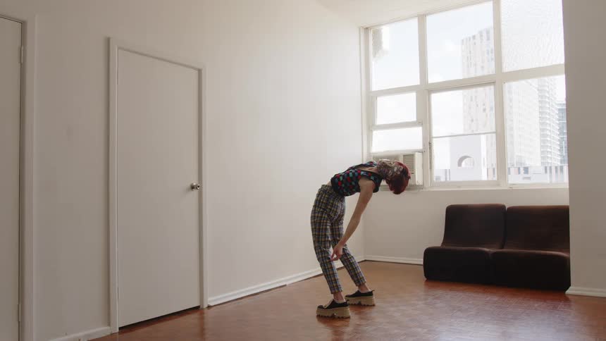 Woman bends forward with arms relaxed wearing patterned clothing in an indoor space with a window in the background