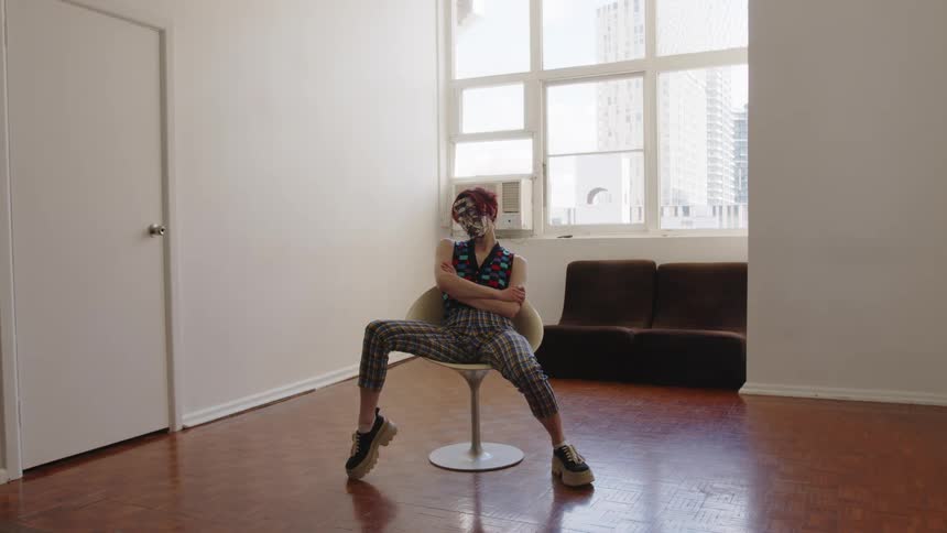 The woman sits while wearing a metallic mask